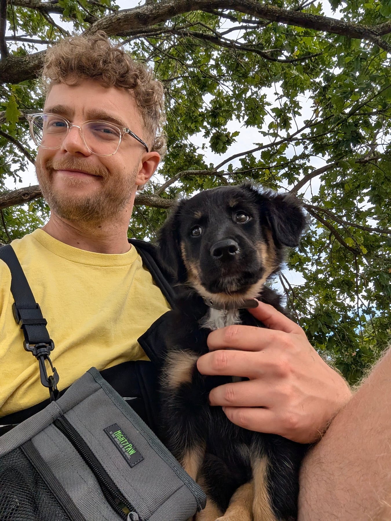 Annie's owner in a yellow t-shirt smiling for a selfie, with Annie in her sling under a big tree