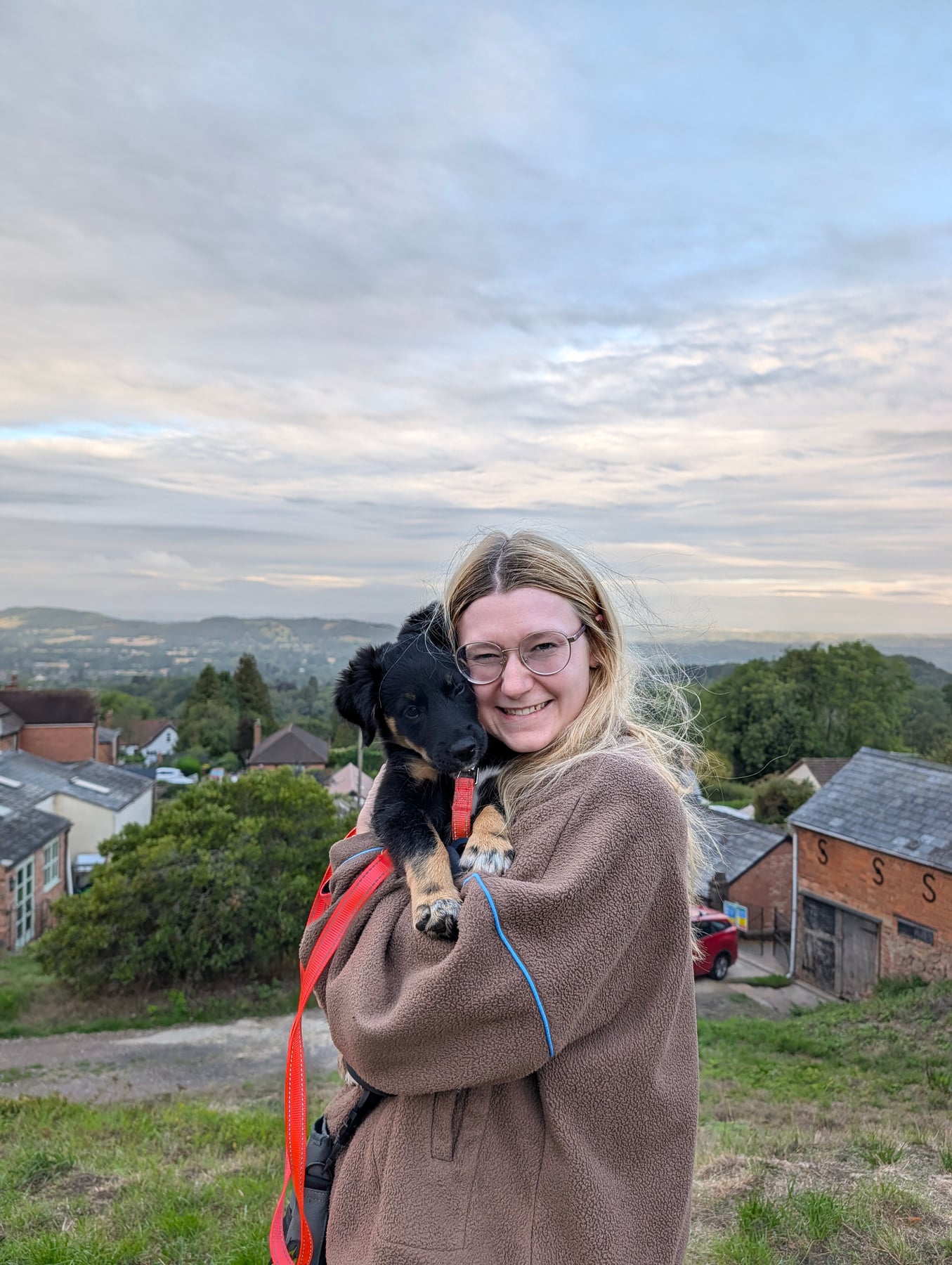 Alisha holding Annie up on a hillside, with the Malvern Hills and a village spread out below them